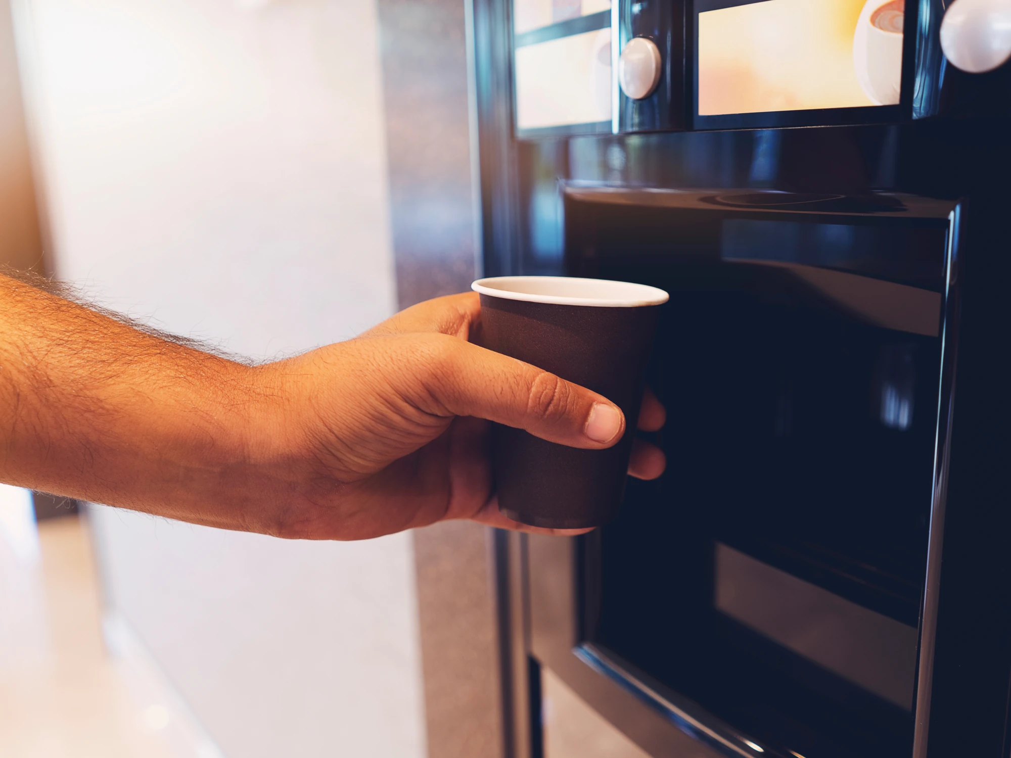 Person putting black disposable cup under coffee machine.